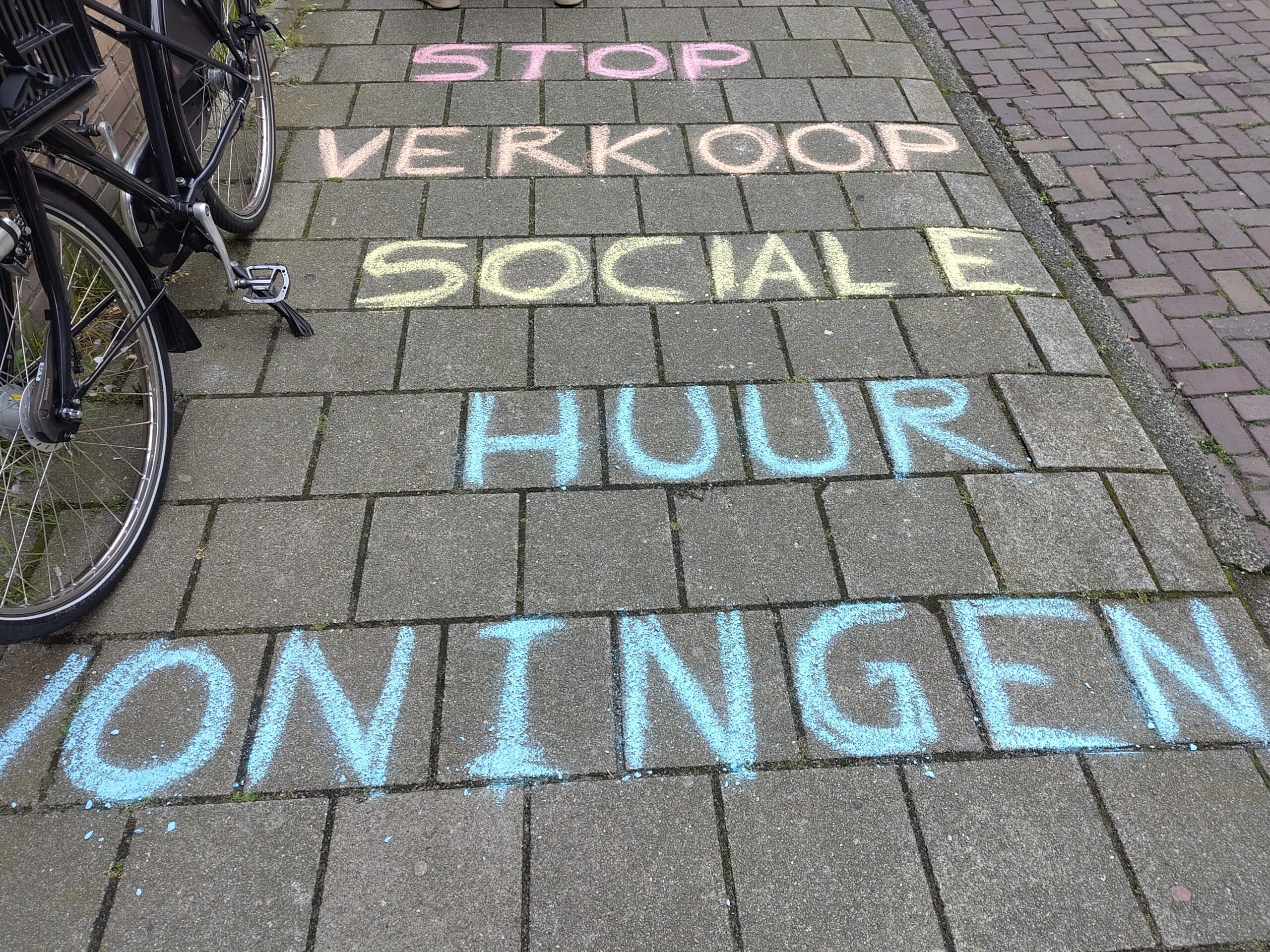 Foto: Met krijt is een leus op de stoep geschreven: STOP VERKOOP SOCIALE HUUR WONINGEN